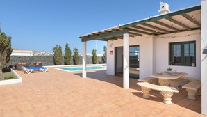 Un espacio al aire libre techado con piscina, sillas de descanso y una mesa de comedor.