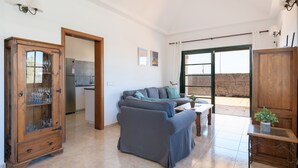 Una sala de estar con un sofá, un mueble con puertas de vidrio, una mesita con una planta, y vistas a un muro de piedra y una puerta.
