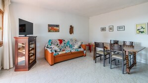 Ein Wohnzimmer mit Sofa, Fernseher, Esstisch, Stühlen und einem Schrank.
