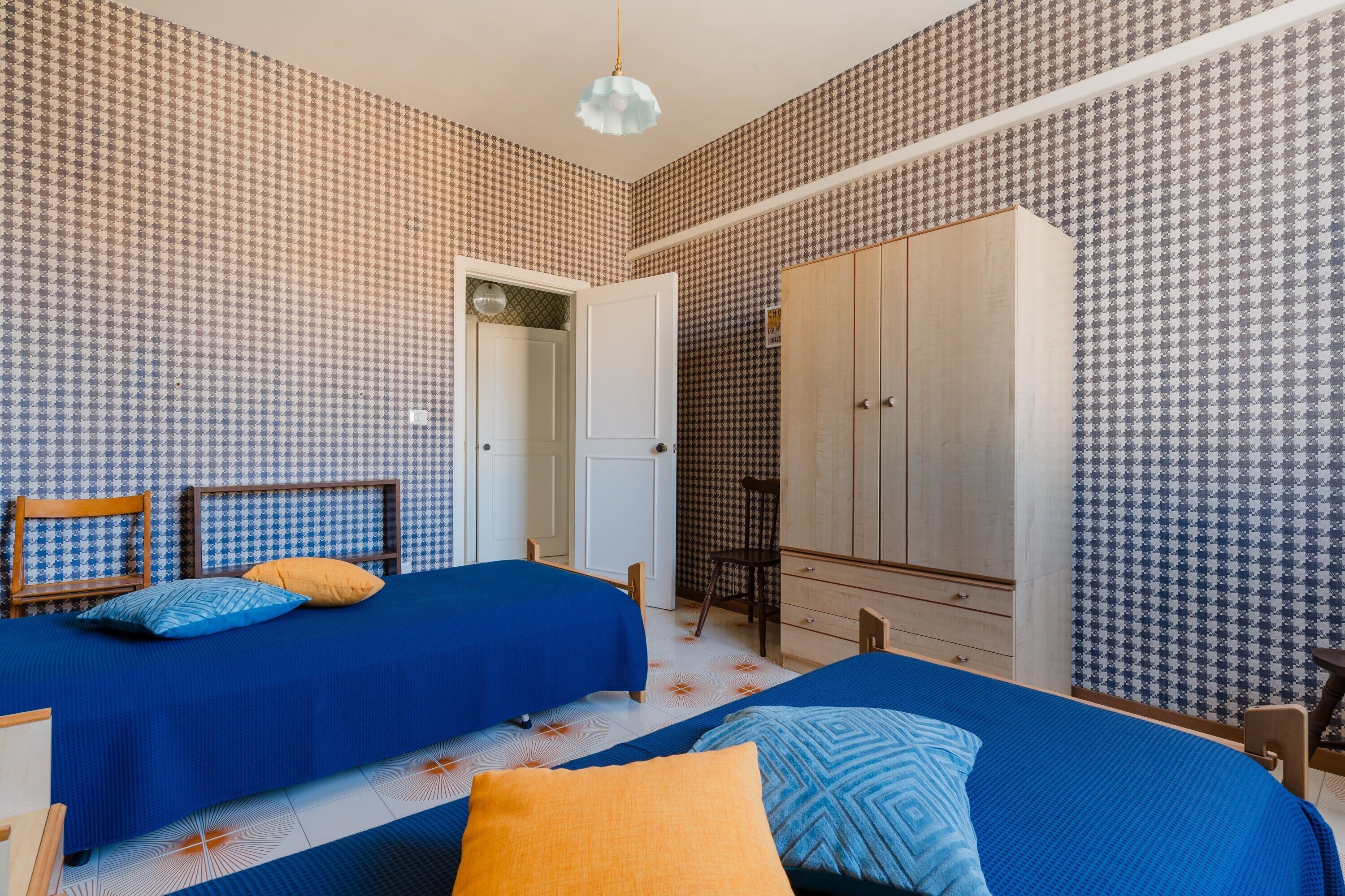 Une chambre avec deux lits, une armoire et une porte donnant sur une autre pièce.