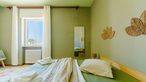 Une pièce comprenant un lit, une fenêtre avec des rideaux, un radiateur, un miroir et un élément décoratif mural.