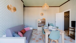 Un salon chaleureux avec un canapé, une table à manger et des chaises, un coin cuisine avec des placards et un téléviseur, et un papier peint à motifs.