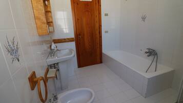 A bathroom with a wooden door, a sink, a bidet, and a bathtub.