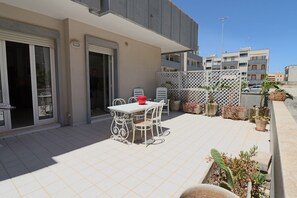 An outdoor patio with a table and chairs, a sliding glass door, and potted plants.