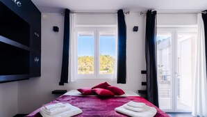 Een hotelkamer met een bed, een televisie, een raam met gordijnen en uitzicht op groen.