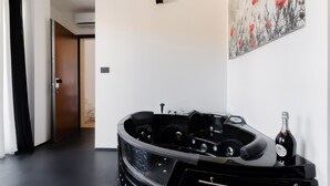 Een moderne kamer met een zwart whirlpoolbad, een fles champagne en een schilderij van een klaproos aan de muur.