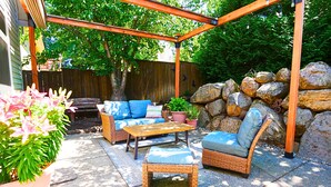 Une terrasse extérieure avec des meubles en osier, une table en bois et un mur en pierre.