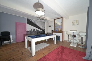 A room with a pool table, a red carpet, a pink door, and a cityscape mural.
