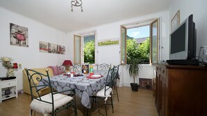 A dining area with a table set for four, a television on a stand, and a window with a view of greenery. - Guest House 'Jolie Chambre Au Calme À Auzat' with Mountain View (Auzat)