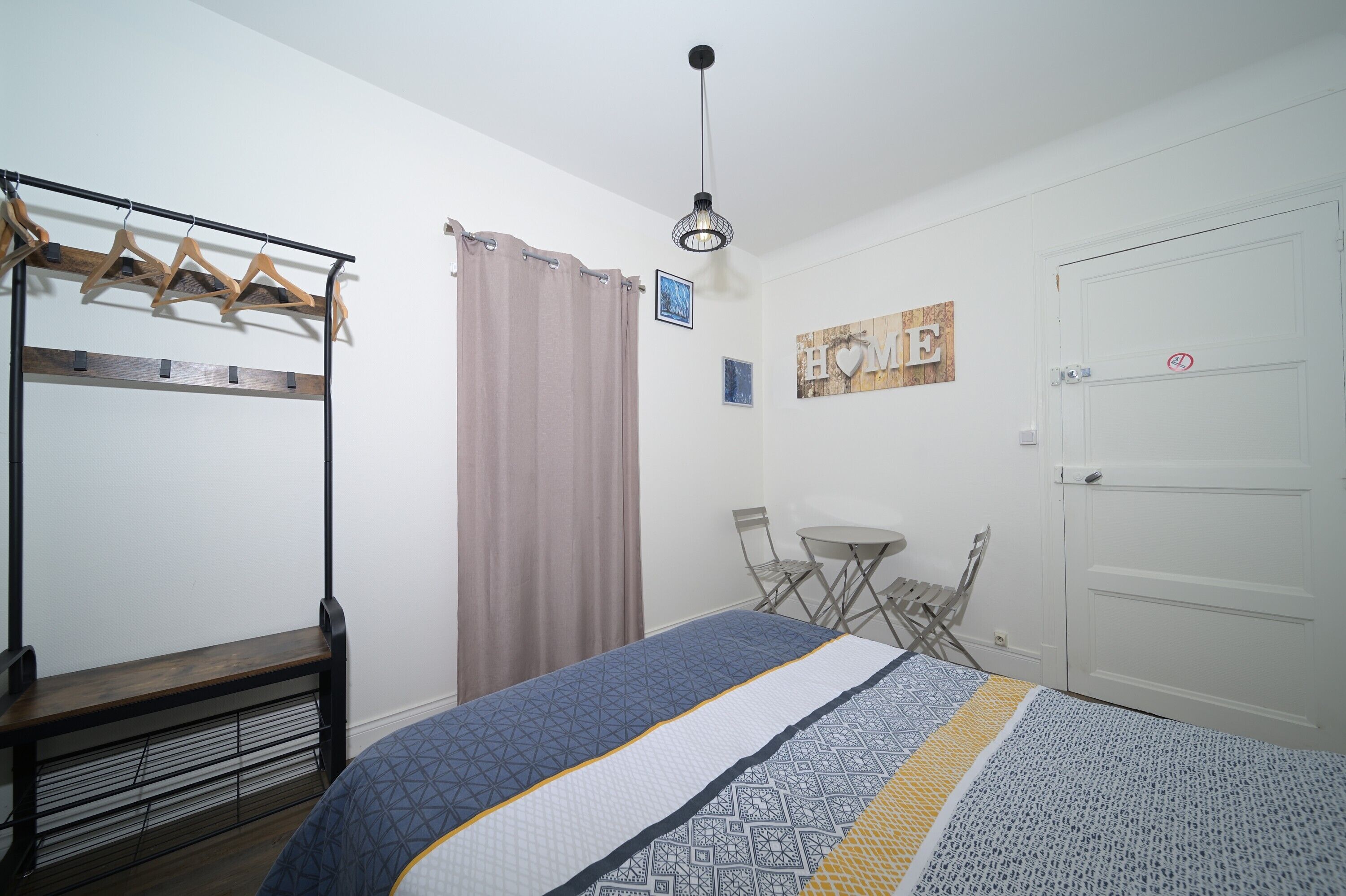 Un dormitorio con una cama, un banco, un perchero, una puerta y una mesita.
