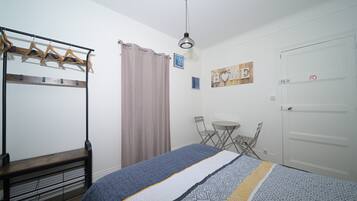 Un dormitorio con una cama, un banco, un perchero, una puerta y una mesita.