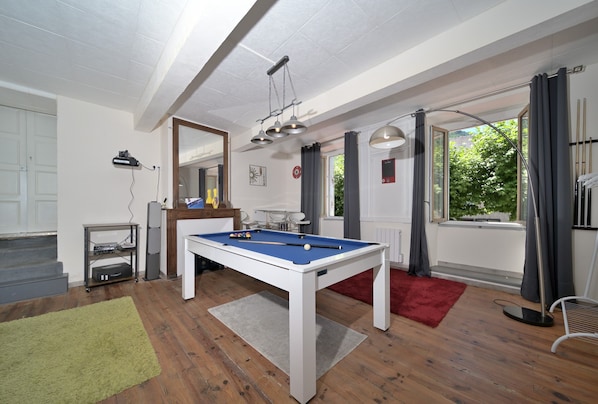 A room with a pool table, a mirror, a window with curtains, and a red rug.