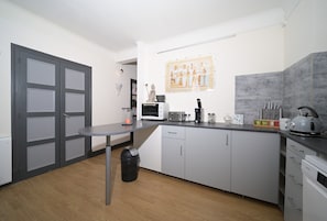 A modern kitchen with grey cabinets, a microwave, a kettle, and a small table.