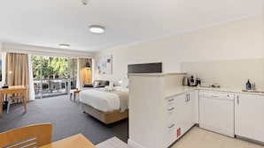 A hotel room with a balcony, a bed, a desk, and a kitchenette.