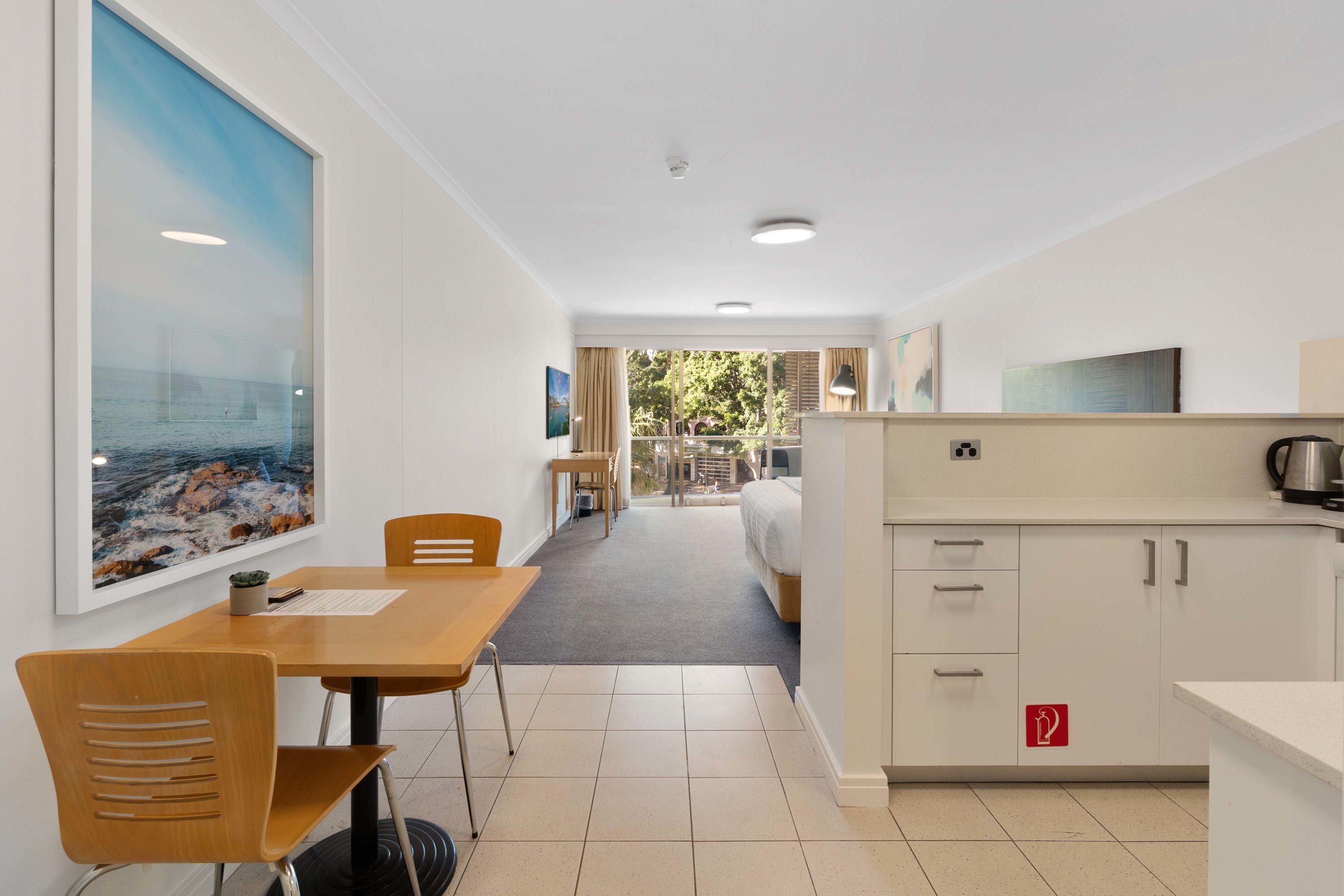 A modern hotel room with a dining area, kitchenette, and a large window with a view of the sea.