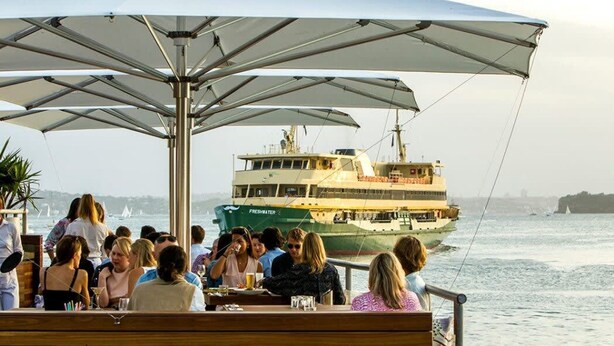 A boat named 'Freshwater' docked at a waterfront restaurant with patrons seated under umbrellas. - Manly Seabreeze With 1 Bathrooms (Manly)