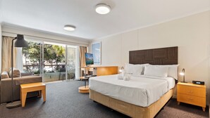 A hotel room with a large bed, a desk, a chair, a small table, a nightstand, and a TV. - Manly Seabreeze With 1 Bathrooms (Manly)
