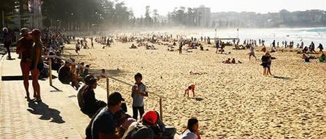 Une plage bondée, où l’on voit des gens assis et se promener le long du rivage.