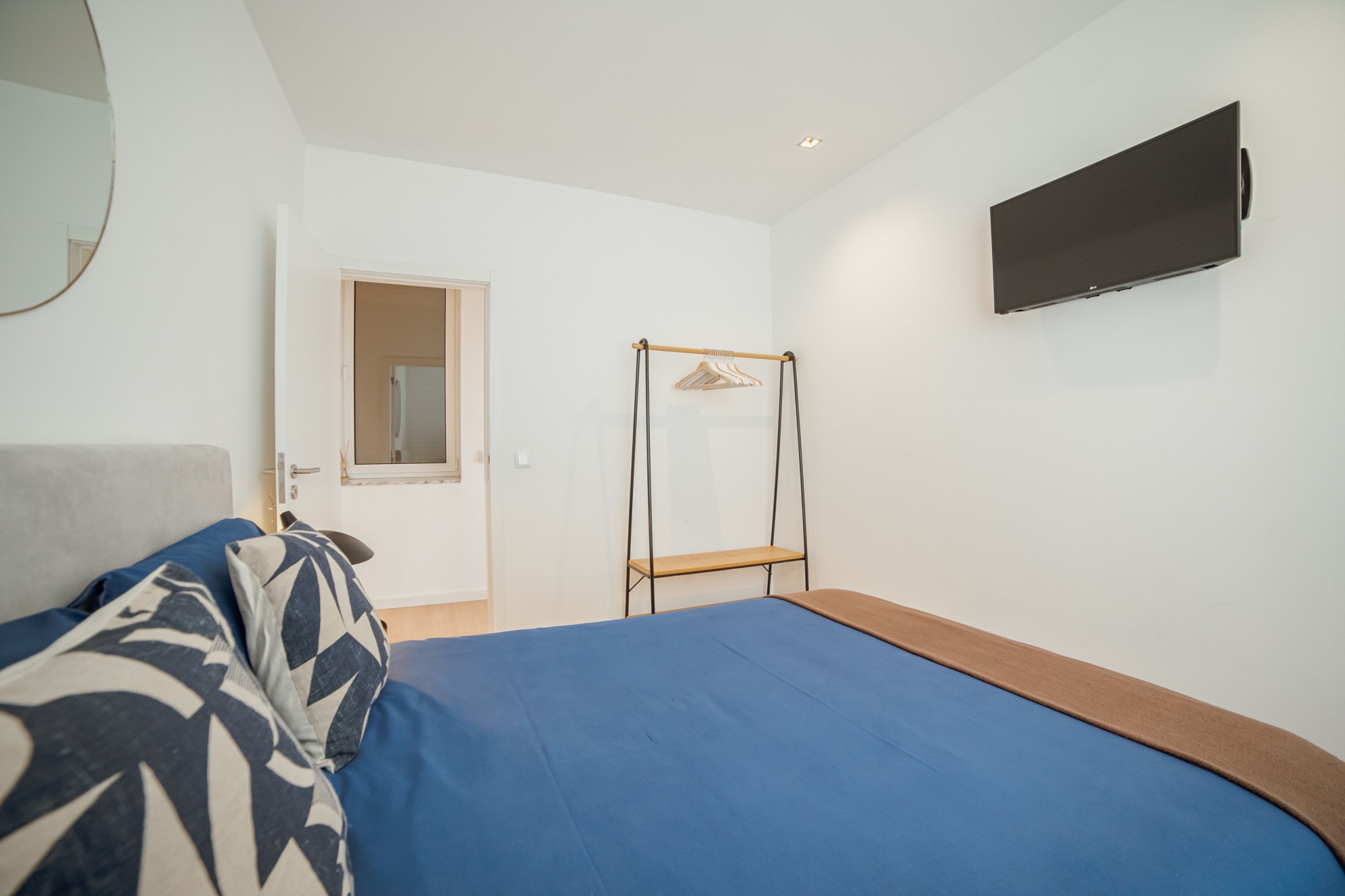 A bedroom with a bed, a wardrobe, a television, and a mirror.