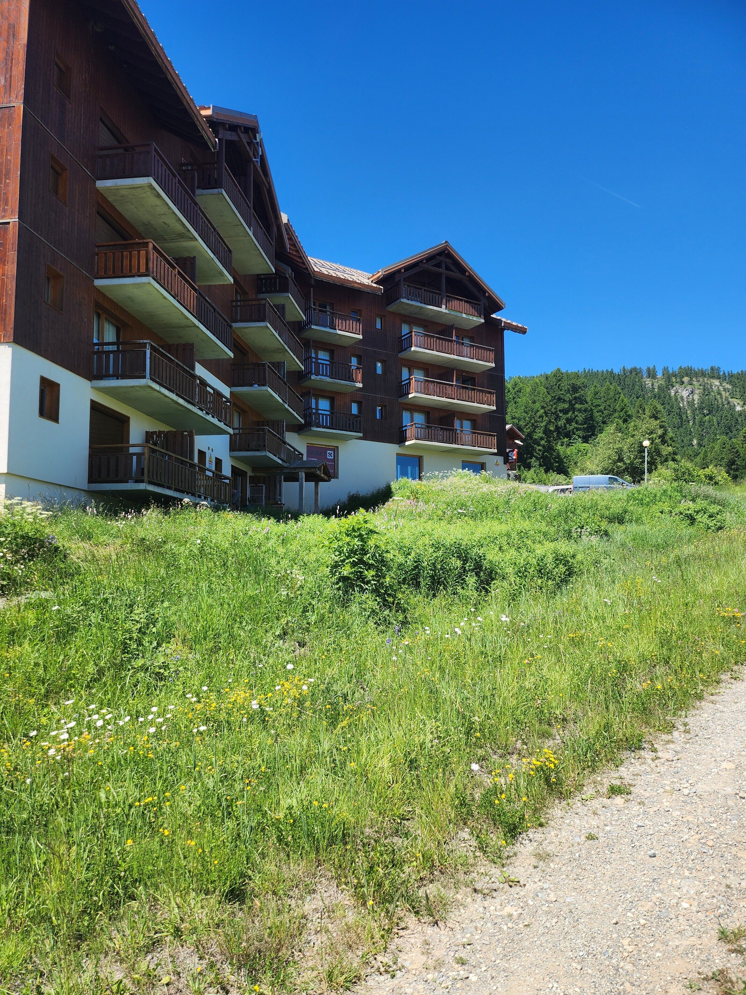 Ein mehrstöckiges Gebäude mit Balkonen, einem unbefestigten Weg und einer Bergkulisse.