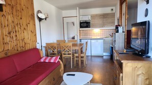 Un espacio habitable pequeño con un sofá rojo, una mesa de comedor de madera y una televisión.