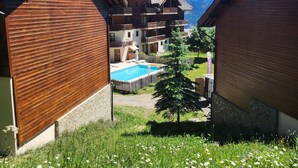 Un edificio de estilo chalet con piscina, rodeado de un exuberante jardín y montañas al fondo.