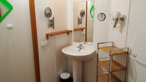Une salle de bain équipée d’un lavabo, d’un miroir, d’un porte-serviettes et d’une petite étagère en bois.