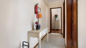 Un couloir avec une console blanche, un extincteur, un certificat encadré et une plante en pot.