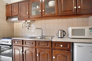 Une cuisine dotée de meubles en bois, d’un évier en acier inoxydable, d’un four à micro-ondes, d’un four traditionnel et d’une machine à café.