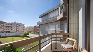 Un balcon avec une chaise en bois, une petite table et une vue sur les immeubles voisins.