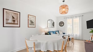 A modern living room with a round dining table, white chairs, a sofa, a TV, and framed nautical artwork. - Air-conditioned rental in Cogolin for 4–6 guests near St Tropez (Cogolin)