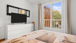 A bedroom with a TV on a white dresser, a window with curtains, and a view of the outside. - Air-conditioned rental in Cogolin for 4–6 guests near St Tropez (Cogolin)