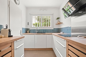 Une cuisine moderne avec des armoires blanches, un plan de travail en bois, un four encastré et une fenêtre donnant sur un paysage verdoyant.