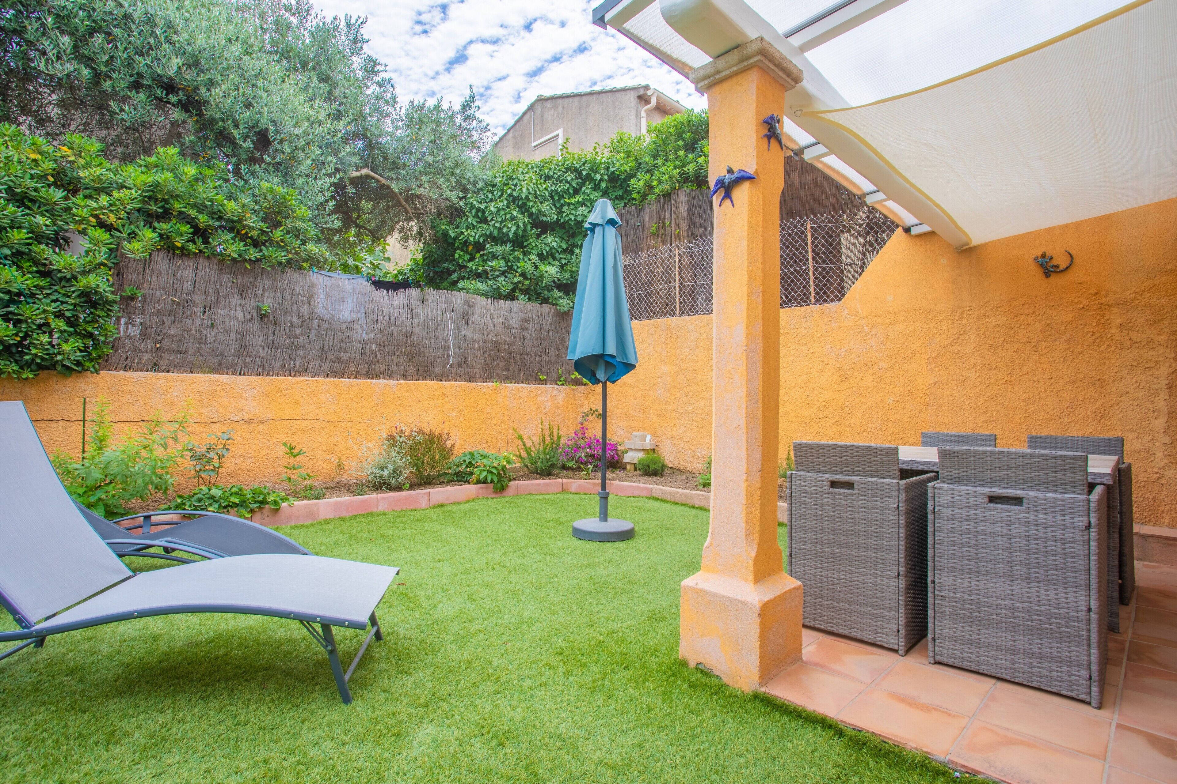 Une terrasse avec un fauteuil de relaxation, un petit parasol et des meubles en osier.