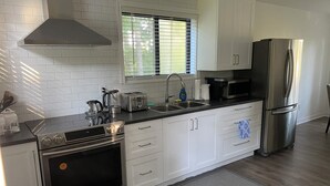 Une cuisine moderne avec des meubles blancs, des appareils en acier inoxydable et une fenêtre équipée de stores.