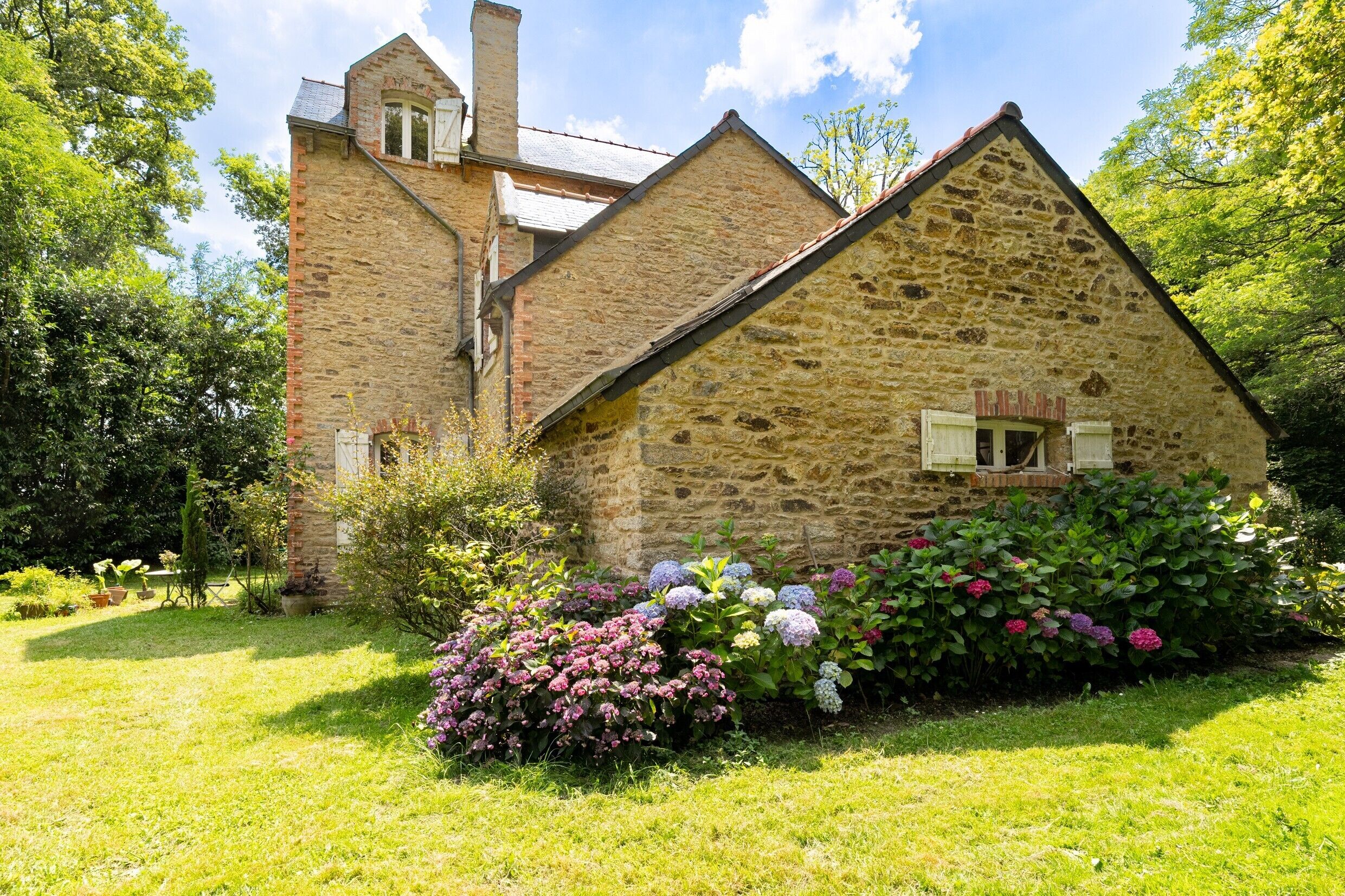 A stone building with a pitched roof, a chimney, and a small window with shutters.