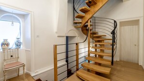 Eine Wendeltreppe mit Holzdielen und Metallgeländern, ein Stuhl und ein Fenster mit Dekoration.