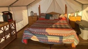 Ein Zelt mit einem Bett, einem Holztisch und einem kleinen Schrank.