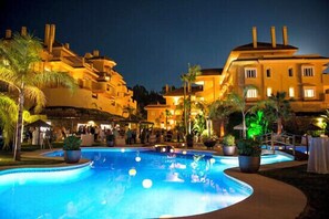 A pool area with a curved edge, surrounded by palm trees and potted plants. - Apartment Aloha Hill Club Marbella (Marbella)