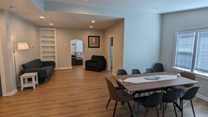 Un salon moderne avec un plancher en bois, une table à manger avec des chaises, un canapé, une lampe et un couloir menant à une autre pièce.