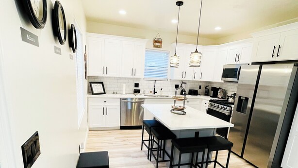 Una cocina moderna con armarios blancos, un refrigerador de acero inoxidable y una isla central con taburetes de bar.