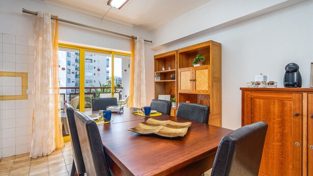 A dining area with a wooden table, chairs, a coffee machine, and a view through a window.