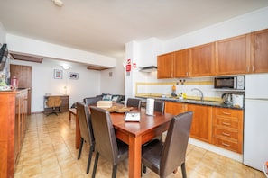 A modern kitchen with wooden cabinets, a dining table with chairs, a microwave, and a refrigerator.