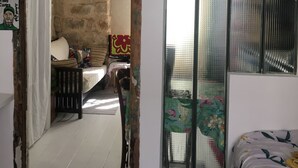 A room with a bed, a chair, a small table, a window with a metal screen, and a doorway leading to another room. - Petit nid D'amour, au Coeur du Père Lachaise (Paris)