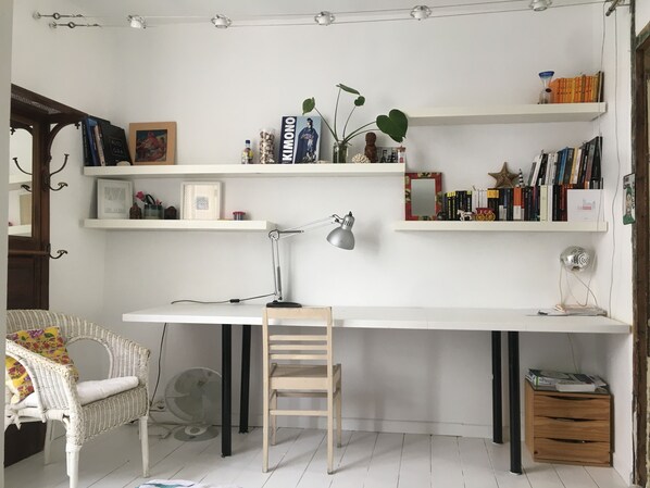 Study area with a large desk, wicker chair, and wooden side table.