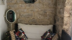 A small, stone-walled room with a bed, a round mirror, a television, and a small table with a tablecloth. - Petit nid D'amour, au Coeur du Père Lachaise (Paris)