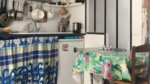 A compact kitchen with a microwave, stove, and various utensils. There's a small refrigerator, a dining table with a floral tablecloth, and a red rug. - Petit nid D'amour, au Coeur du Père Lachaise (Paris)