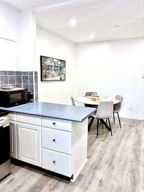 Cozinha moderna com armários brancos, bancada de granito e área de refeições com mesa e cadeiras.