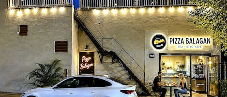 A white car parked in front of a building with a sign reading 'Pizza Balagan.'