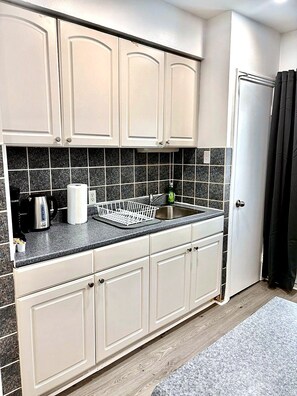 A kitchen with white cabinets, a granite countertop, a stainless steel sink, and a black tiled backsplash.